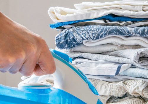 Front view of female hand holding a steam iron, pile of folded clothes in background