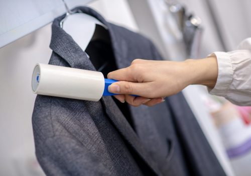 Clean blazer. Female hand with white lint roller moving along dark jacket cleaning, face is not visible